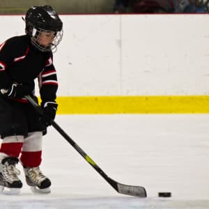 picture of young child learning to skate ice hockey with a hockey stick