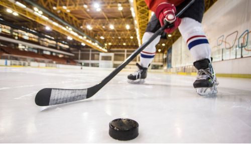 Hockey player with a stick and puck on Ice, showing why hockey players tape their sticks