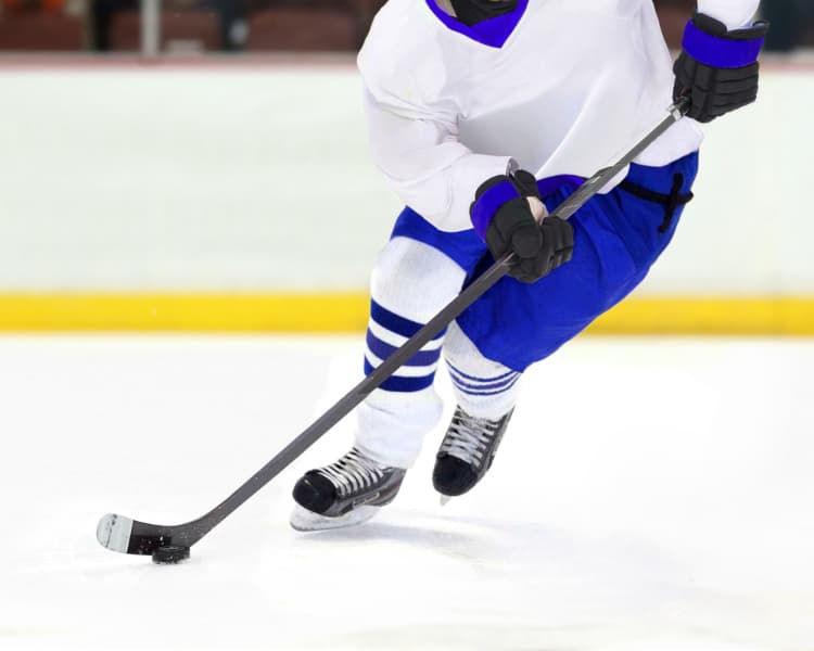 Picture of Ice Hockey player skating with a puck down the ice rink. Player wearing white and blue uniform