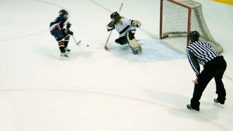 Referee watching carefully as Youth Ice Hockey player attempts shootout and Goalie attempting to block the shot