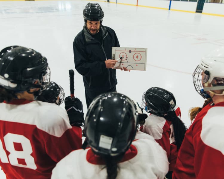 Coach with youth ice hockey team showing a white board of a forecheck strategy