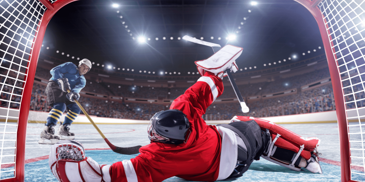 Goalie dressed in red stopping a puck from opposing player 